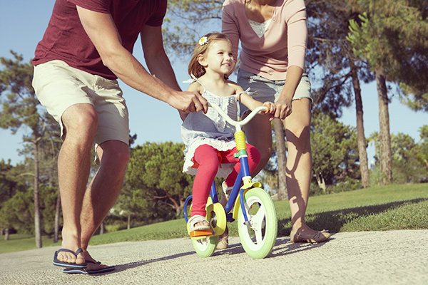 Parents Teaching Daughter To Ride Bike In Park