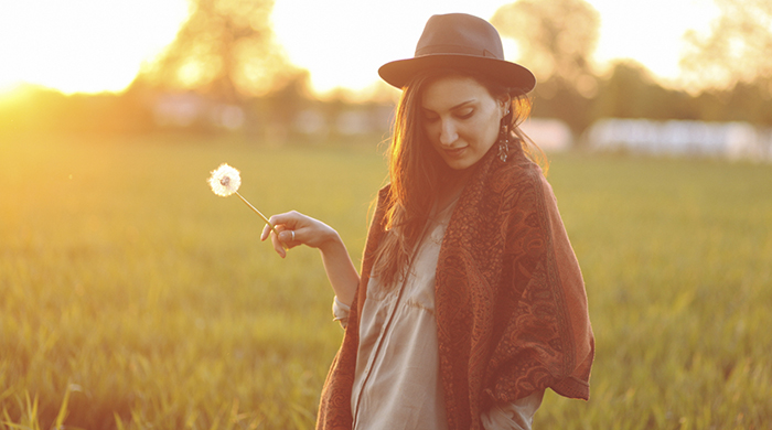 Girl wearing hat in a field holding a dandelion