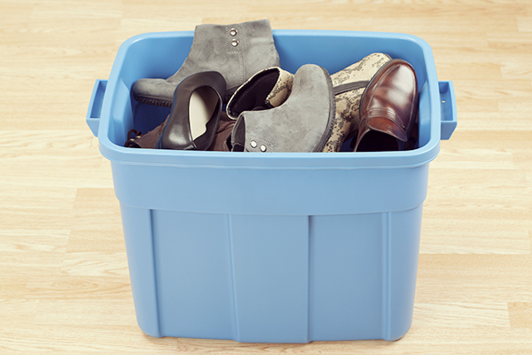 Plastic storage box filled with a variety of shoes on a hardwood floor.