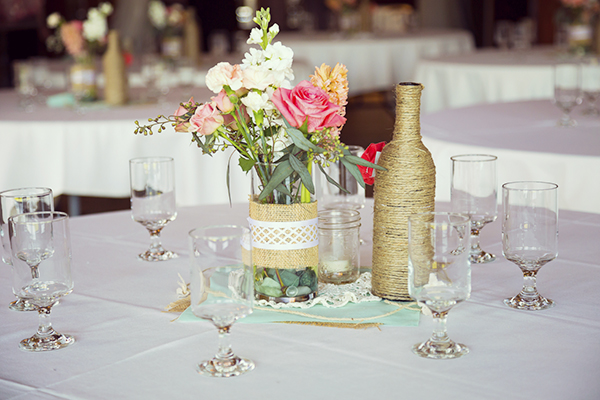 DIY wedding decor table centerpieces with wine bottles wrapped in burlap twine and rose flowers.