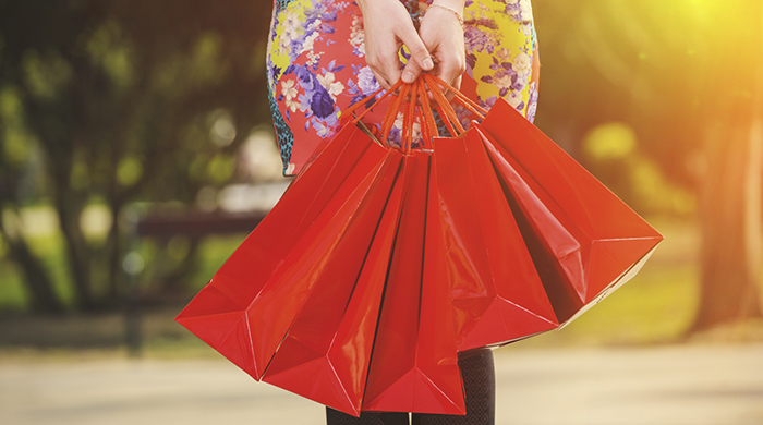Woman in floral dress holding red shopping bags