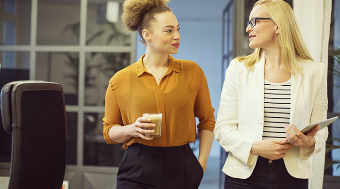 Two female colleagues discussing work while walking alongside each other in office