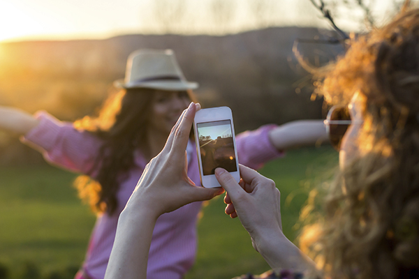Woman taking photo with smartphone of friend outside