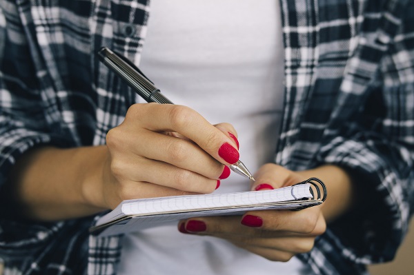 Woman in plaid shirt and a red manicure pen writing in a noteboo