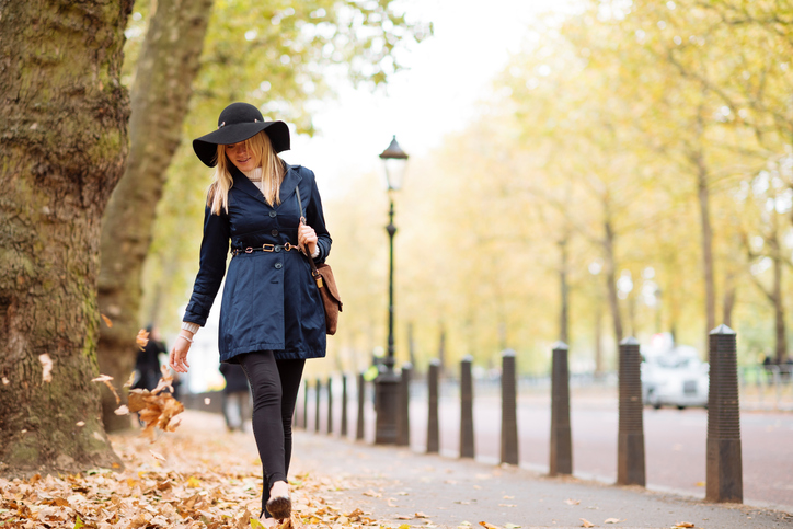 Stylish young woman strolling through autumn leaves in city park