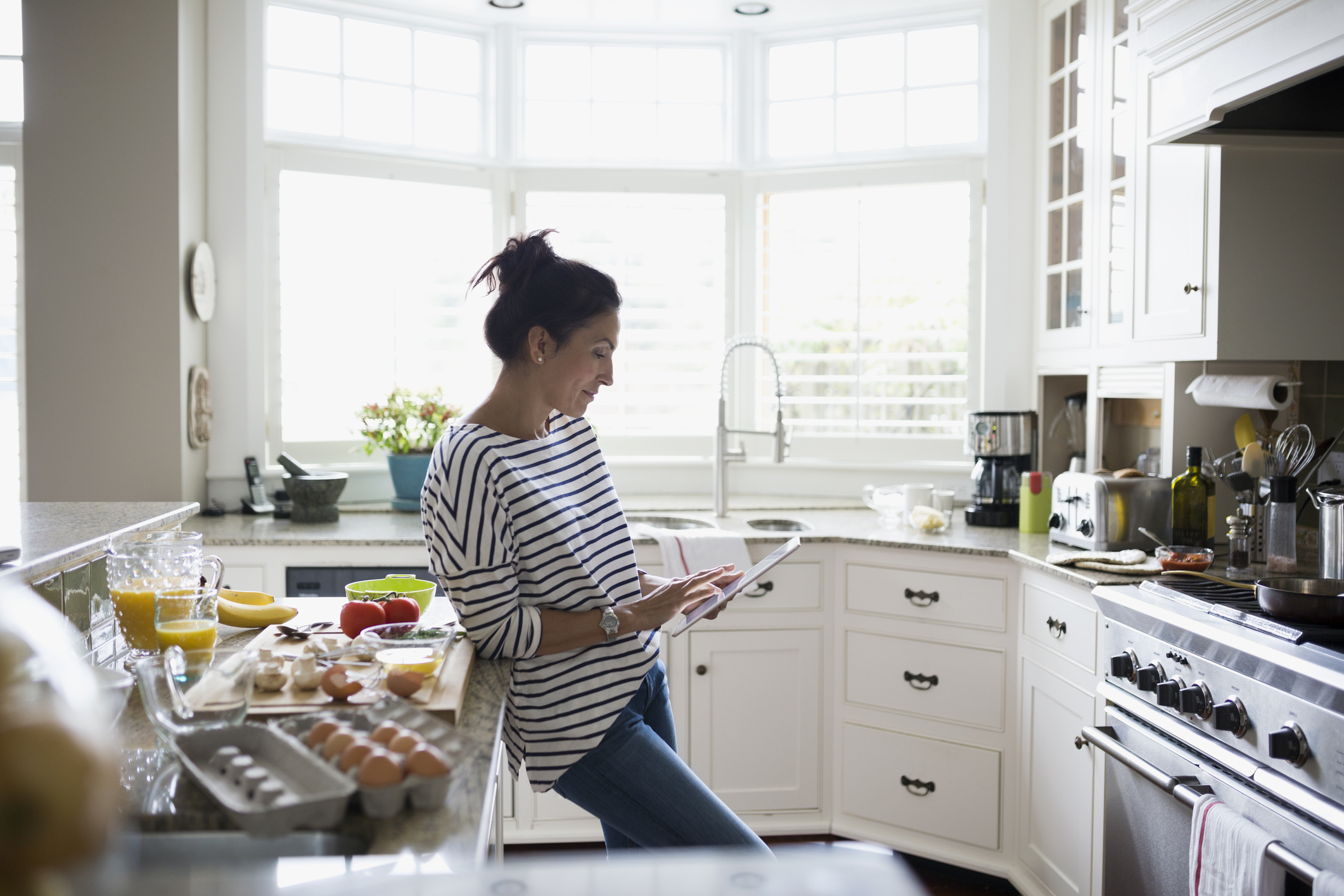 Woman cooking in kitchen looking up recipe on tablet