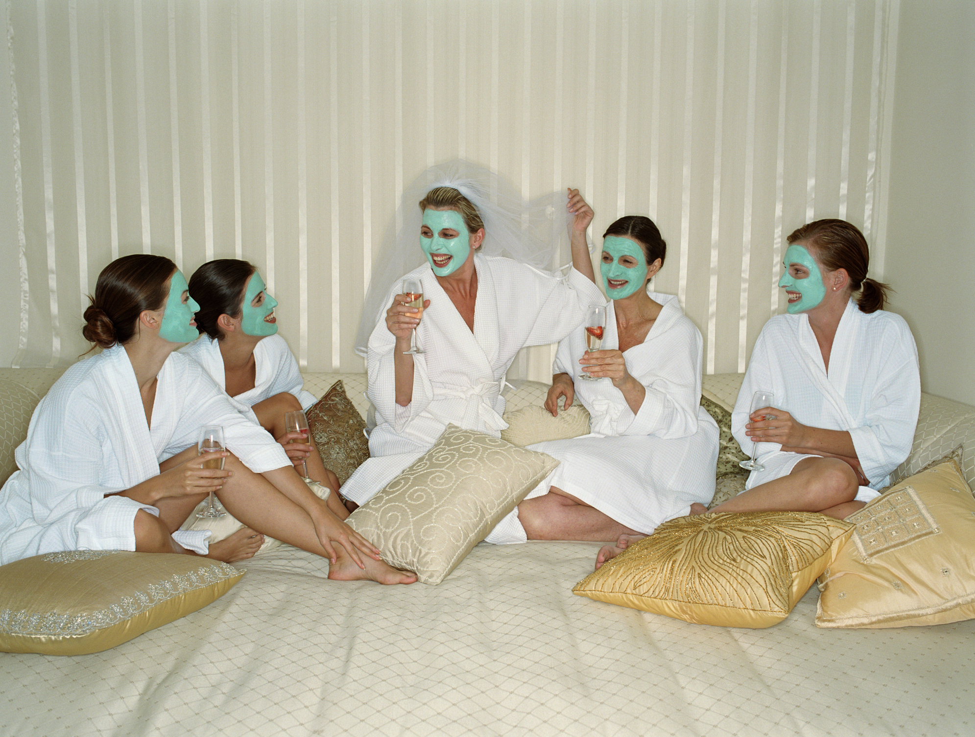 Five women in face masks holding champagne glasses, one wearing veil