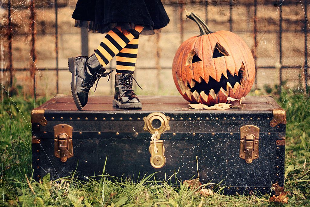 Little girl standing on a trunk next to a jack-o-lantern