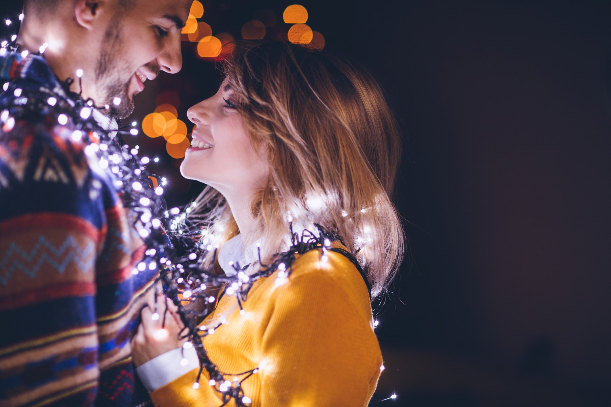 Couple in sweaters with lights wrapped around them