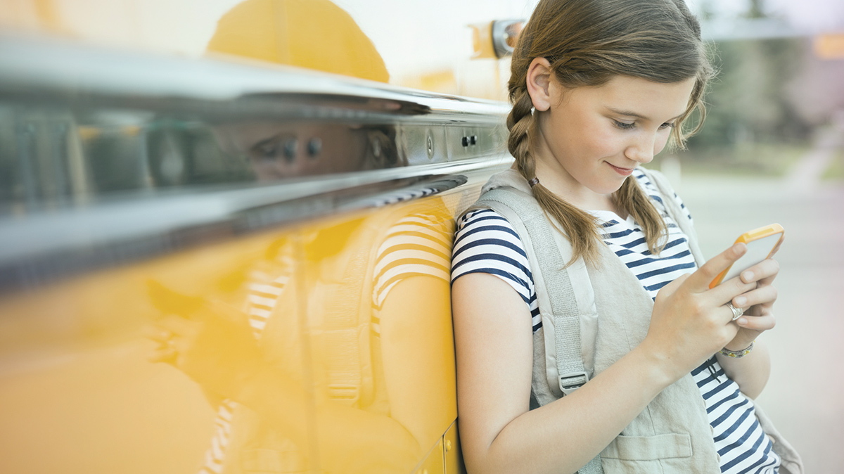 Girl leaning against a school bus, looking at her phone