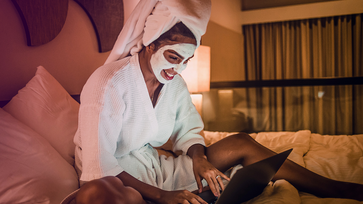 Girl in a robe and face mask looking at laptop